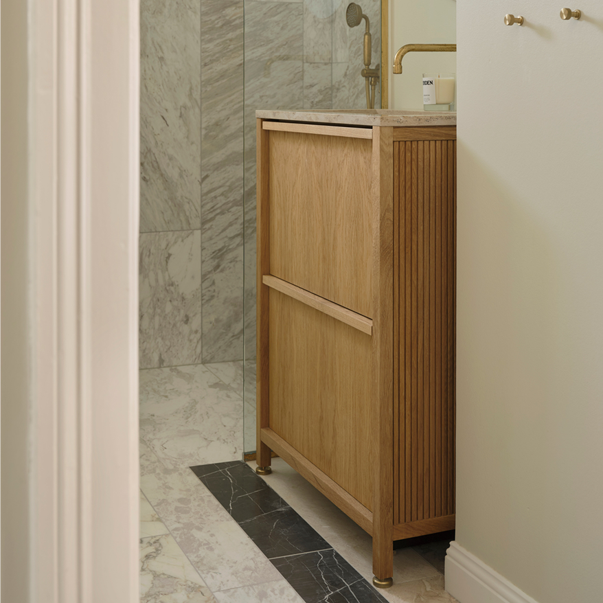 Mueble de baño en madera con frente acanalado junto a un muro de piedra